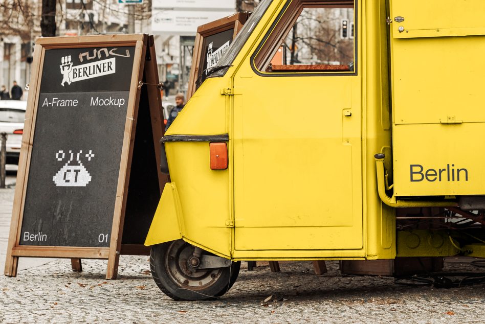 Yellow vintage food truck parked next to a chalkboard A-frame mockup with pixel art, urban street setting, ideal for branding and design mockups.